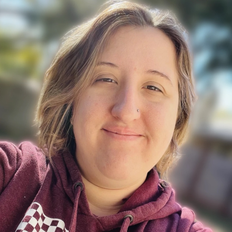 Jax smiling at the camera outdoors, in a maroon hoodie with a white checkerboard print.